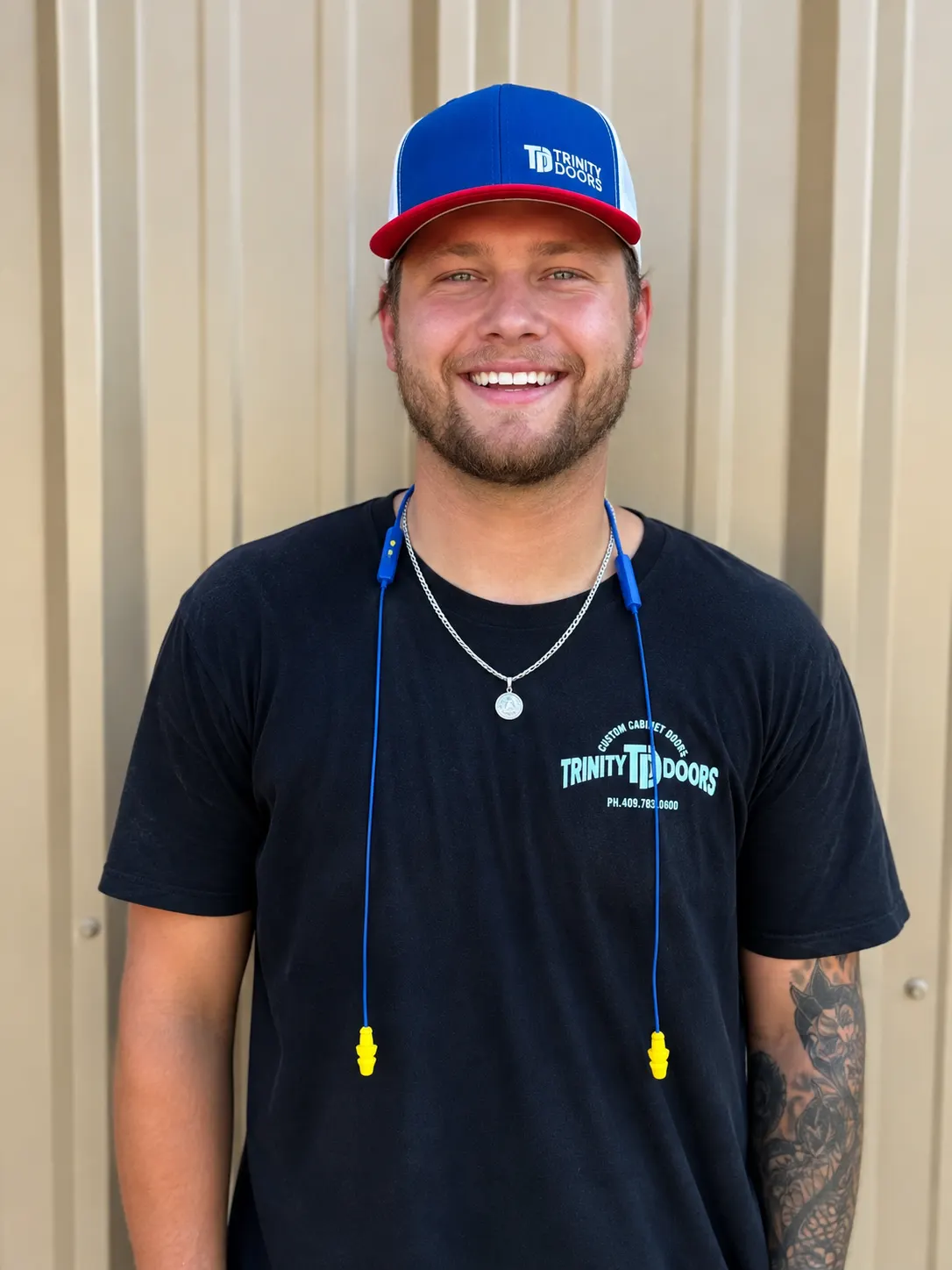 A smiling Trinity Doors production team member in a company shirt and cap outside the Vidor, TX shop